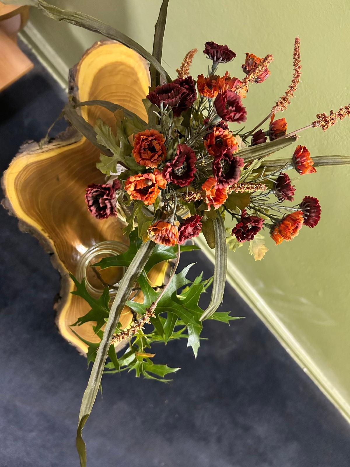 Autumn flowers and oak leaves arranged on a wooden slice