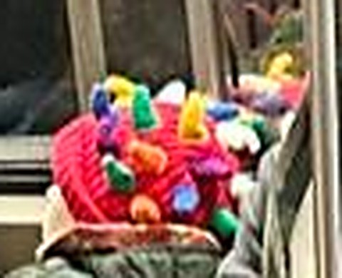 Child’s red knit cap dotted with multicolored cone heads on the subway