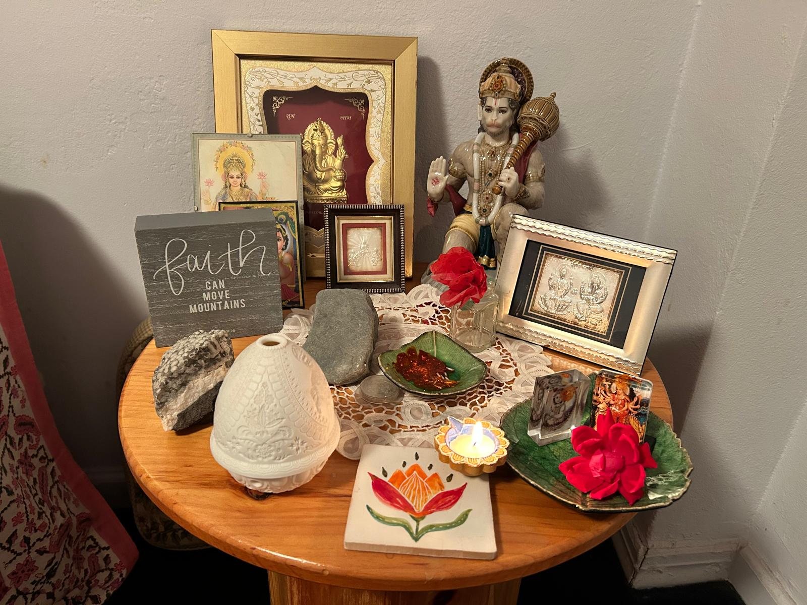 Home altar with lit diya, red rose and gods for Navami pujan